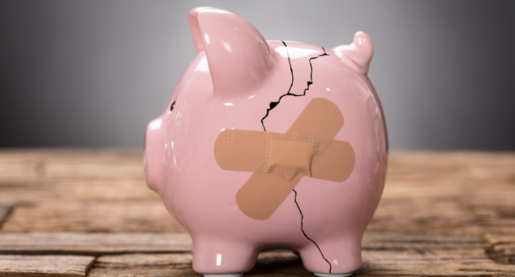 Small piggy bank with cracks in it, taped together with two bandages